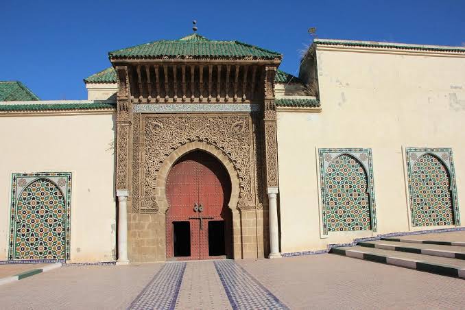 The interior of the Mausoleum of Moulay Ismail in Meknes — zellige-lined anteroom leading through arched doorways toward the tomb of the great Alaouite sultan who made Meknes his capital, one of the few sacred Islamic interiors in Morocco open to non-Muslim visitors